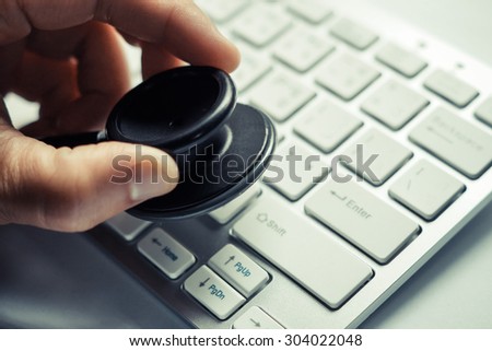 hand using a stethoscope over computer keyboard - computer system check and maintenance concept