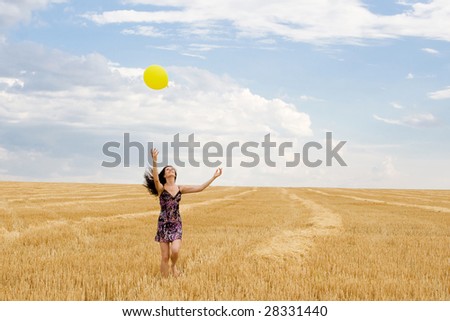 a sexy happy woman playing with yellow air ball on the straw  field under beautiful sky with clouds.