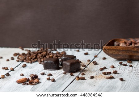 handmade chocolates without heat treatment lie on old wooden table with cracked paint the surface, wooden cup with cocoa beans. raw food diet concept.coffee cocoa beans grated cinnamon. rustic style