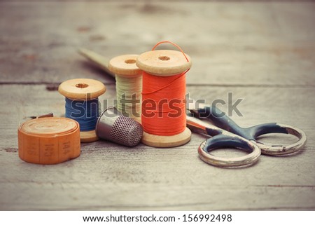 tailor\'s tools - the old scissors, spools of thread, tape centimeter, thimble on a wooden background