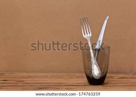 Knife and Fork. Knife and fork in a glass on a wooden table over grunge background