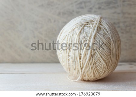 White ball of yarn on a wooden table over vintage wallpaper. Ball of knitting yarn