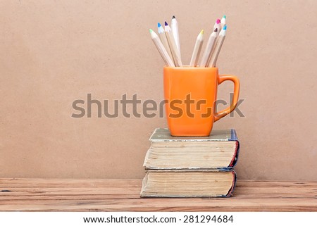 Books tower and orange mug with colored pencils. School theme