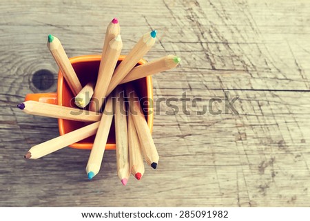 Cup with colorful Pencils on wooden table. Top view. Toned image