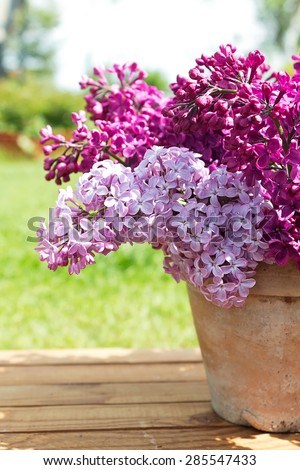 Ceramic pot with a branch of lilac flower on wooden background. Syringa vulgaris