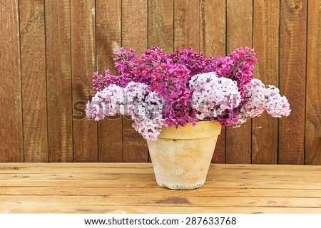 Ceramic pot with a branch of lilac flower on wooden background. Syringa vulgaris