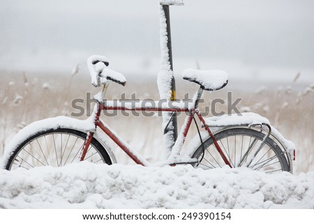 Parked and covered with snow bike at bus stop.