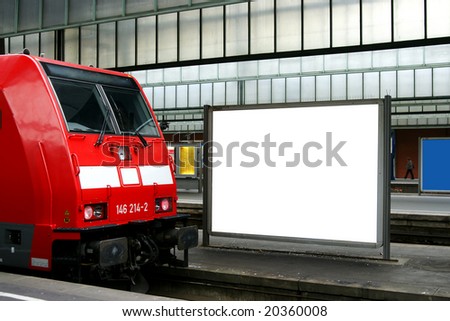 Red commuter train at railway station with blank billboard