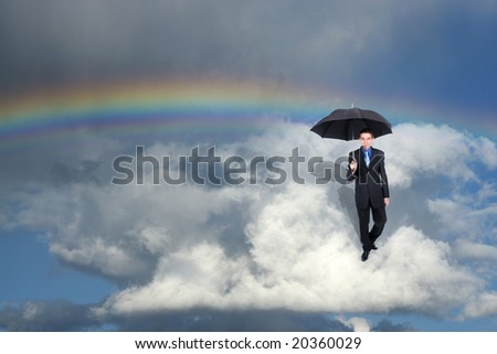 businessman holding an umbrella while wanderin the clous in front of a rainbow