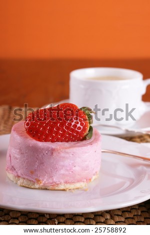 Fresh strawberry fancy cake with half a fruit on top and a cup of hot cappuccino