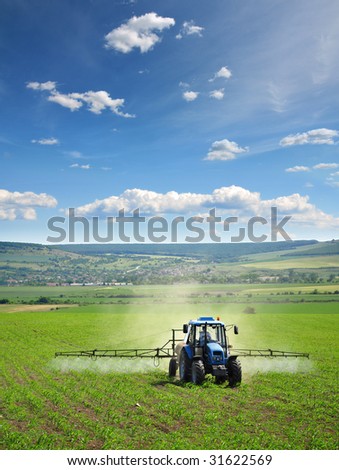 Farming tractor plowing and spraying on field vertical