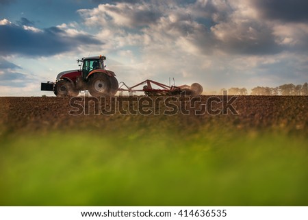 Farmer in tractor preparing land with seedbed cultivator, sunset shot