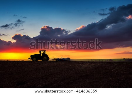 Farmer in tractor preparing land with seedbed cultivator, sunset shot