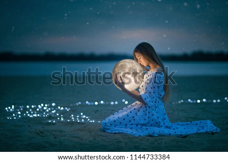 Beautiful attractive girl on a night beach with sand and stars hugs the moon, Artistic Photography