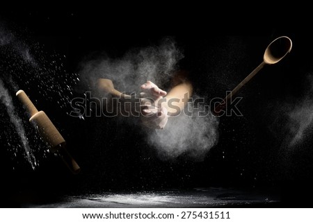 hand clap of chef with wooden rolling pin and spoon in the air with splash flour on black background