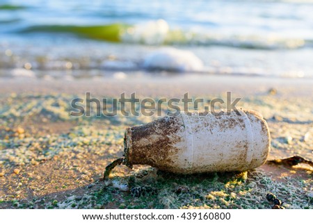 Old and Dirty Plastic Bottle on the beach with water pollution background (green algae bloom)