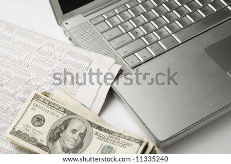 computer laptop and financial section of newspaper and stack of dollar bills
