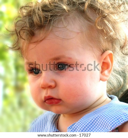 cute face of baby with curly hair and blue eyes and a serious expression in an outdoor setting