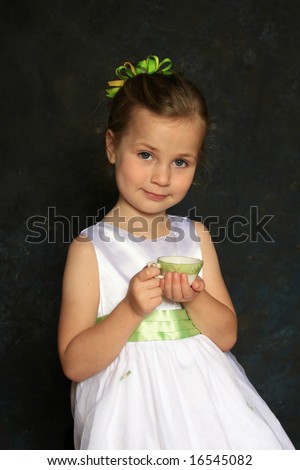 Cute little girl in a white dress holding a tea cup