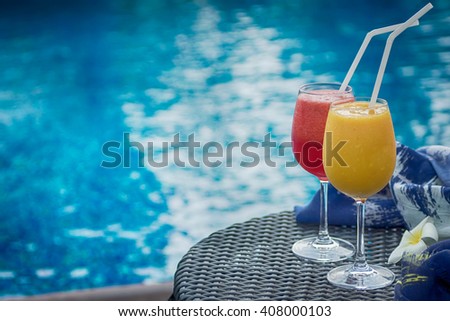 Two cocktails red and yellow on table against blue swimming pool. Travel, luxury, vacation background. Detox healthy drink. Text space