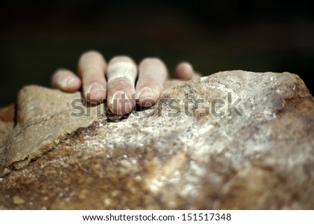 A hand holding onto the edge of a rock while rock climbing.