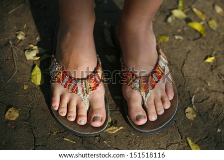 A woman's feet in colorfull slops standing outside.