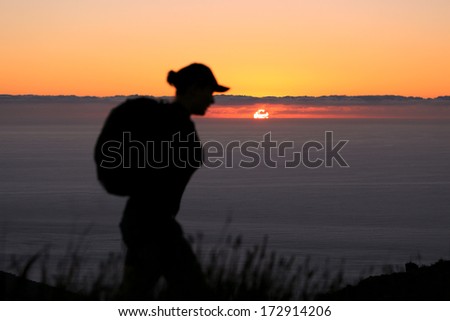 Silhouette of a female tourist enjoying a hike along Table Mountain as the African sun sets in the background.