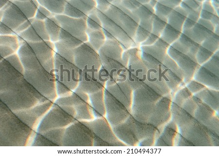 Underwater view of a clear ocean floor with sunlight shining through making a beautiful pattern on the sand.