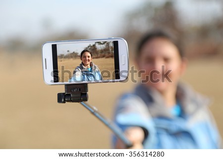 Woman taking a selfie photo with her mobile phone, using a selfie stick.