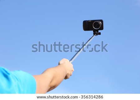 Woman taking a selfie photo with her mobile phone, using a selfie stick.