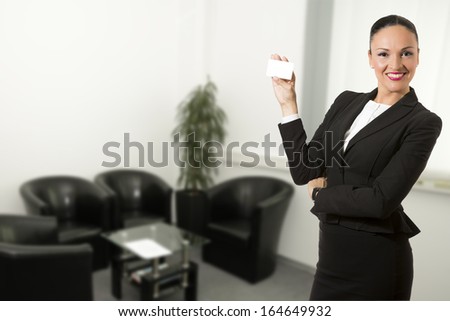 Business dressed woman, standing inside office space and holding white card.