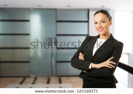 Business dressed woman, hands crossed, smiling in front of the office.
