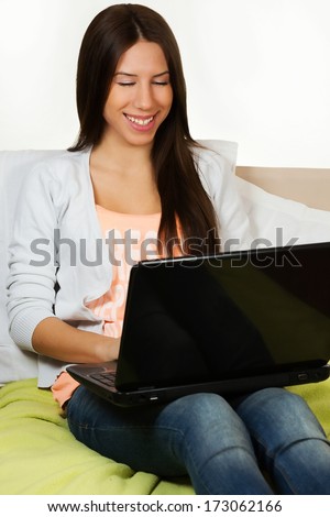 Cute teenage girl, surfing the internet, sitting on her bed.