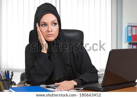 Worired arabic woman, traditional dressed, working at desk inside her office.
