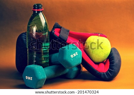 Composition presenting healthy lifestyle,with green apple,boxing gloves,bottle of water and dumbbells,against orange background.