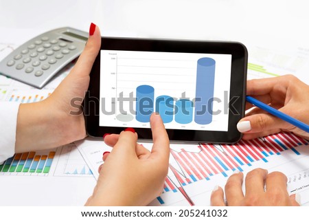 Female hands reading business columns  on tablet, at office desk.