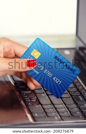 Close up of a female hand holding credit card, in front of laptop keyboard.