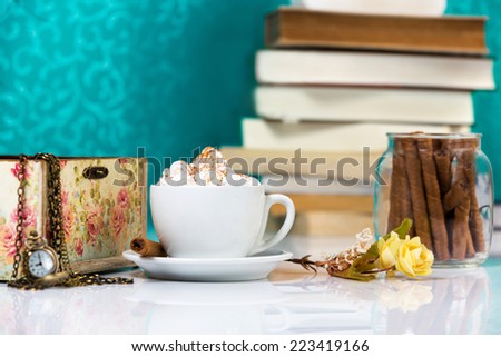 Cup of cappuccino with chocolate rolls and books in background.