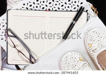 Woman accessories. White purse and shoes next to open note book. Top view.