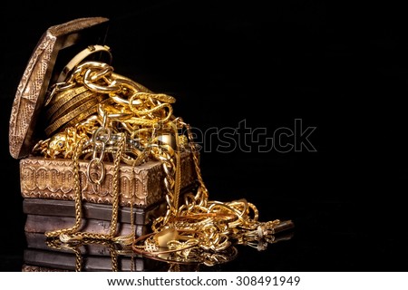 Old wooden chest with pile of various golden jewelry, isolated against black background.