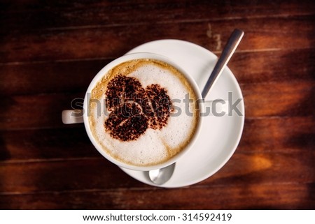Cup of coffee with foam, on top of wooden table. Top view.