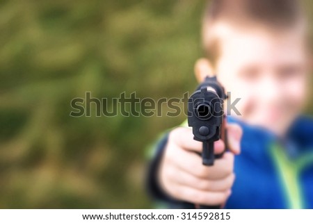 Young boy,holding a toy gun,against green grass background.