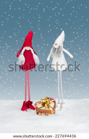 Two christmas elf standing in the snow with a heart shaped christmas gift.