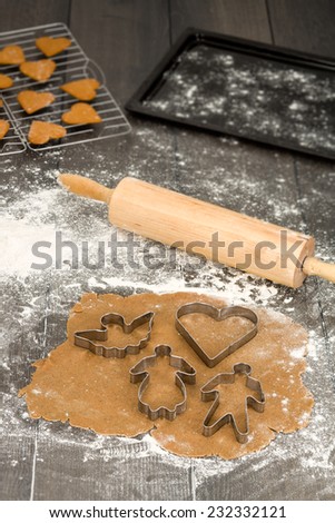 Rolled out gingerbread dough on floured table with rolling pin, wire rack and a baking plate on partly blurred background.