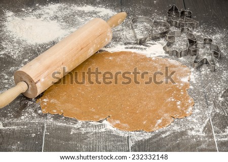 Rolled out gingerbread dough on on a floured dark wooden table with rolling pin and cutters beside.