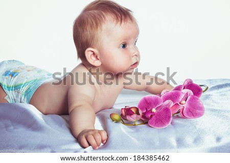 Beautiful blue-eyed baby in diapers lying on white fabric with flower in hands