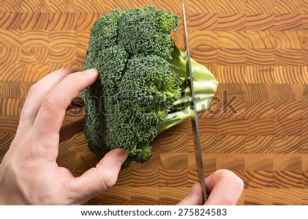 Someone cutting broccoli on a cutting board.