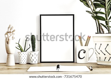 Modern desk with plants in different design pots, notebook, wooden hand, a cup filled with pencils and mock up a frame. The designer workplace of a freelancer.