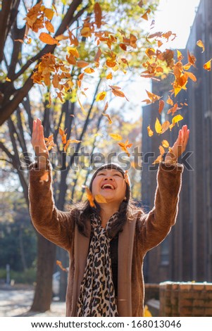 Autumn / fall woman happy throwing leaves up in the air with arms raised up towards the sky with smiling cheerful, elated expression of happiness. Beautiful girl in colorful forest foliage outdoor.
