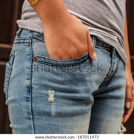 Close up of woman in the gray T-shirt inserting the hand into the blue jeans pocket